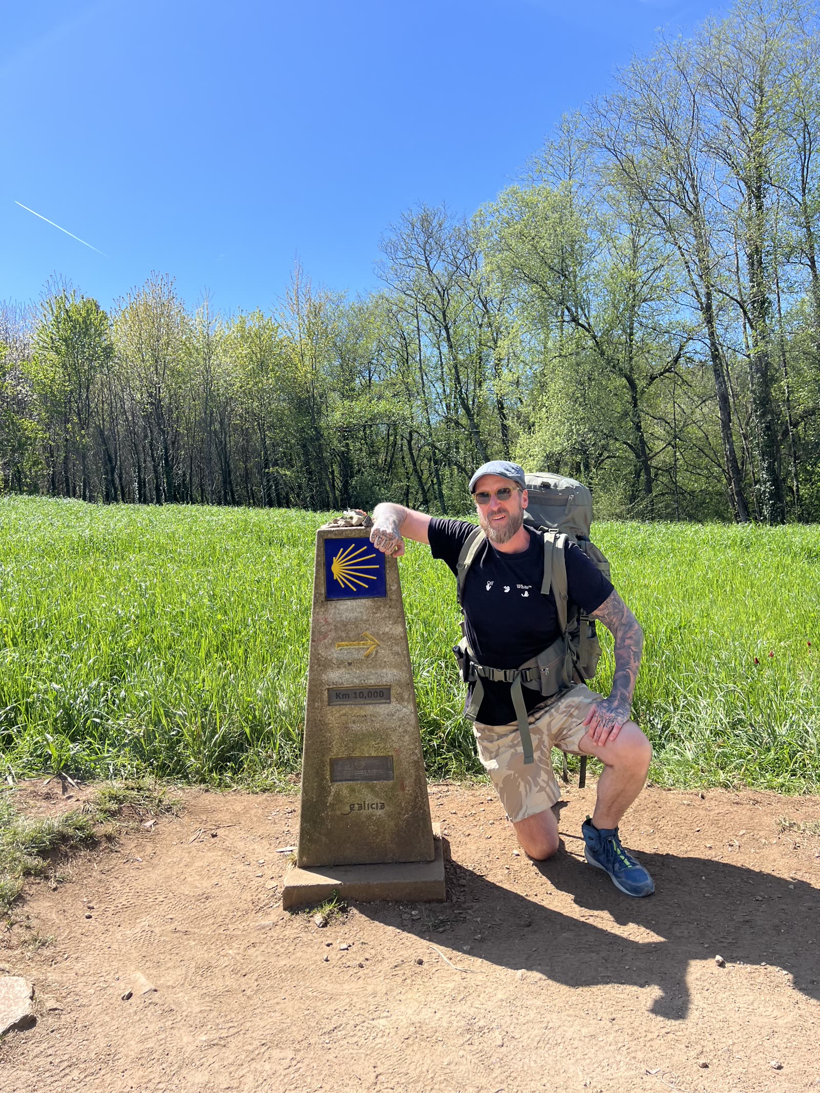 Pontus on the Camino, kneeling beside the Km 10,000 waymark in Galicia